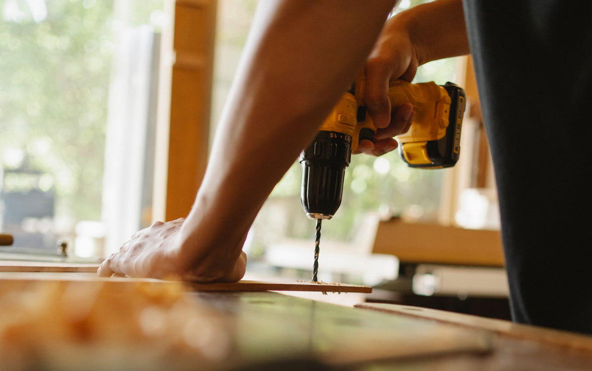 Hands drilling into a wooden board in a home workshop